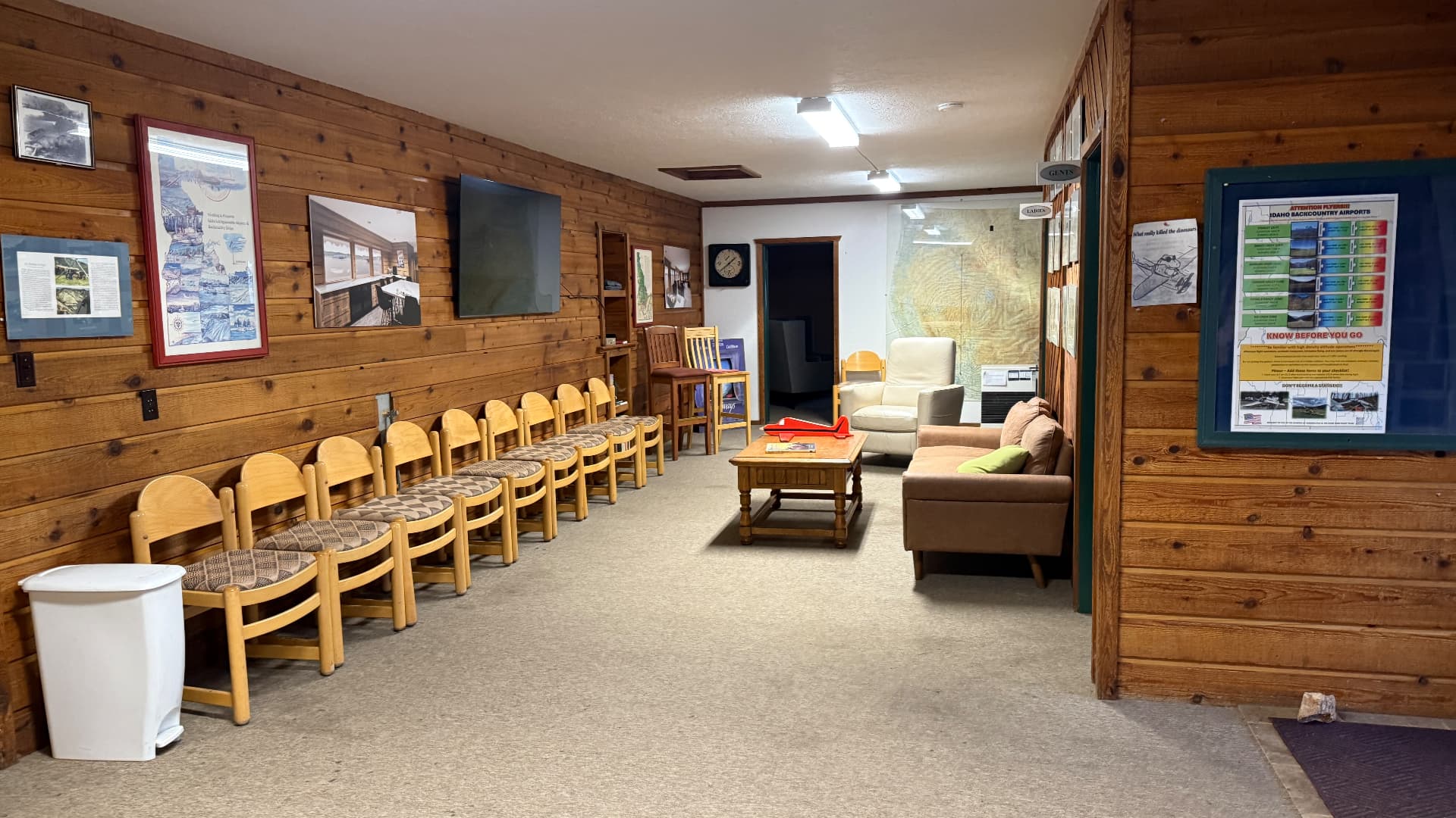 Wood-paneled briefing room with rows of chairs, backcountry airport charts and a wall map