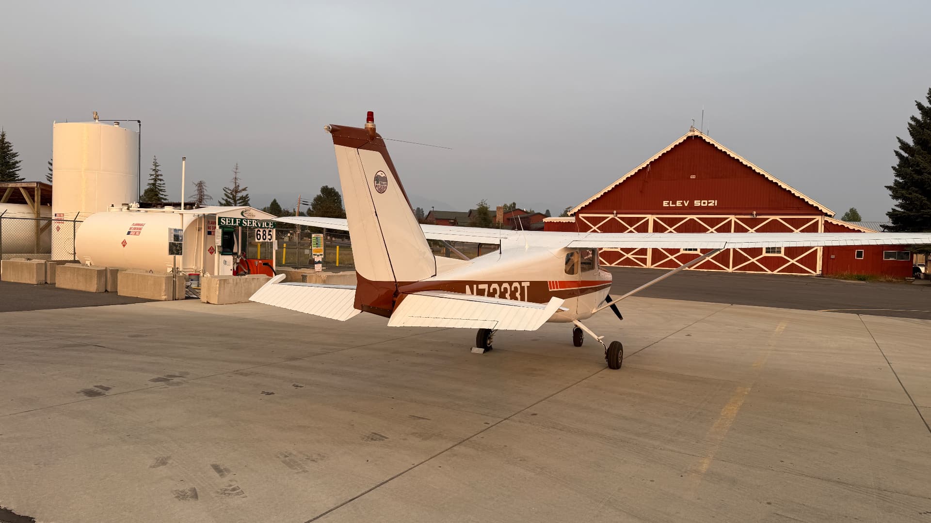 Cessna 172 N7333T parked at the self-service fuel island directly beside the red hangar