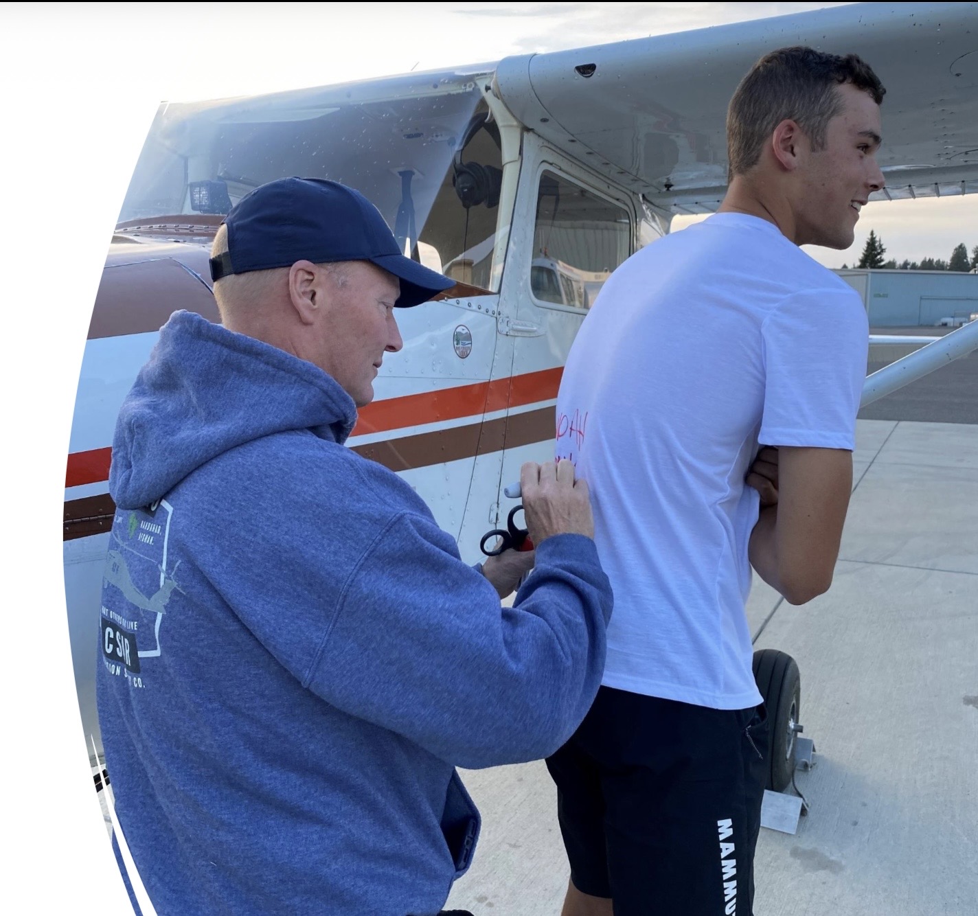 Noah Spangenberg being congratulated by a club mentor beside a Cessna after a flight